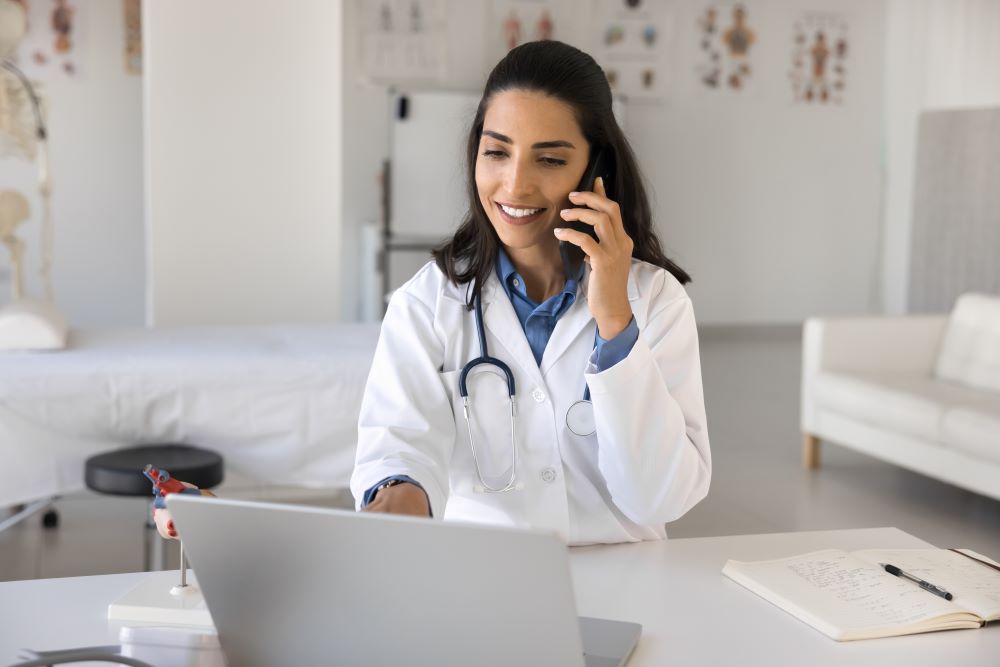 Smiling young woman doctor consulting patient by phone