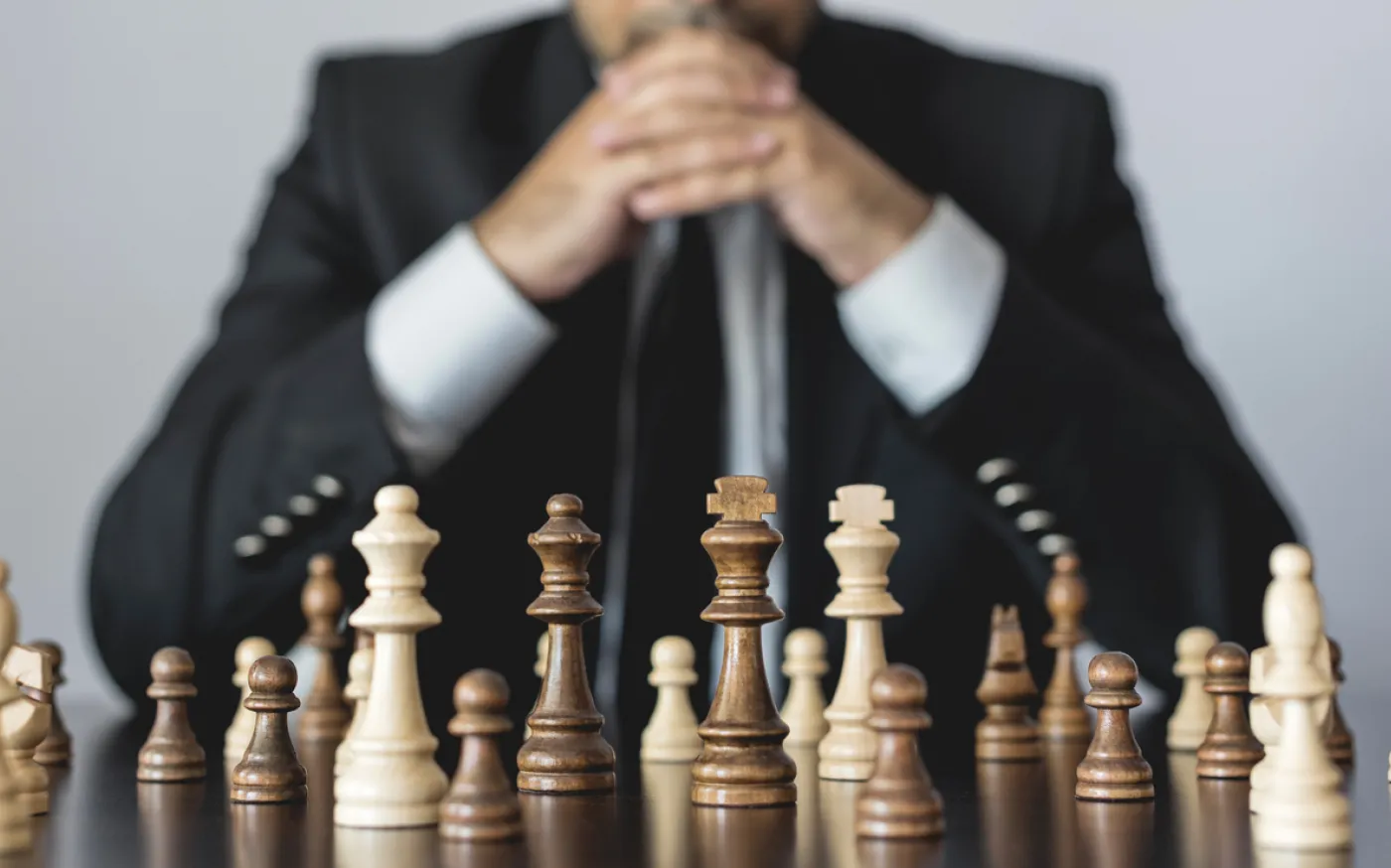 A person in a suit sitting behind a chessboard with their hands together in a "ready to play" position.